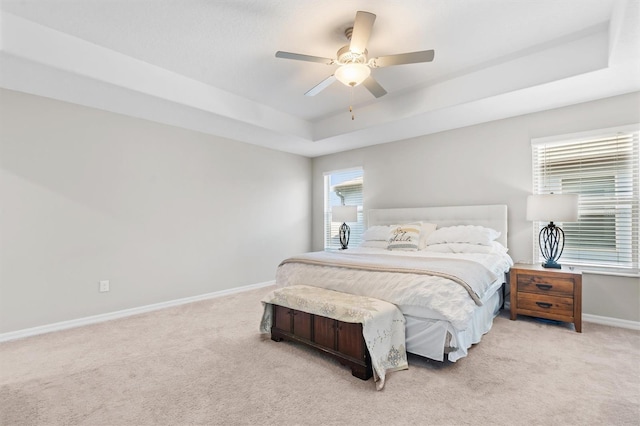 bedroom with light colored carpet, a raised ceiling, and ceiling fan