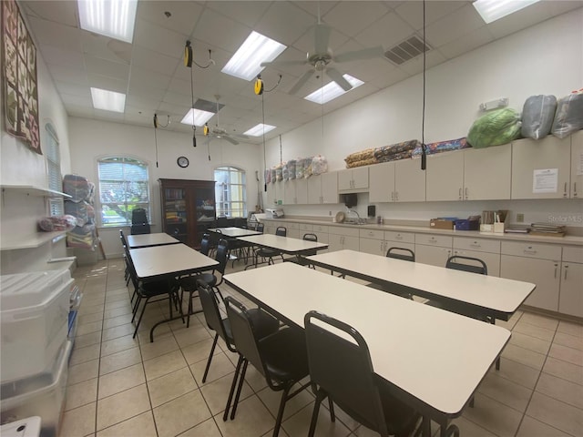 kitchen with an island with sink, white cabinets, light tile patterned floors, ceiling fan, and a towering ceiling