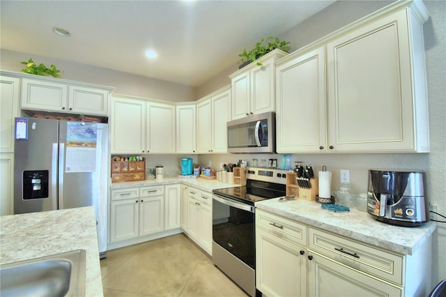 kitchen with stainless steel appliances, sink, cream cabinetry, light stone countertops, and light tile patterned floors