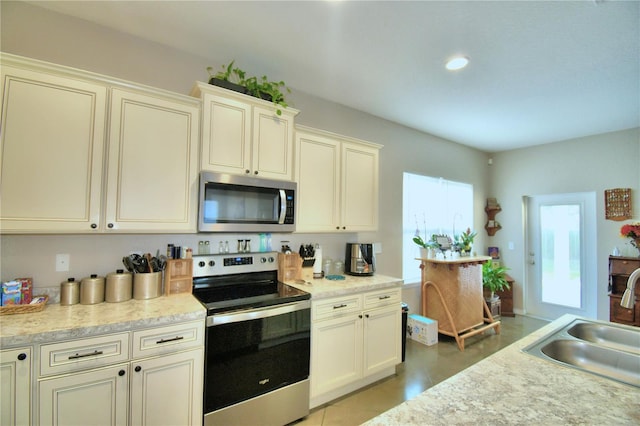 kitchen with sink, light tile patterned flooring, cream cabinetry, and stainless steel appliances