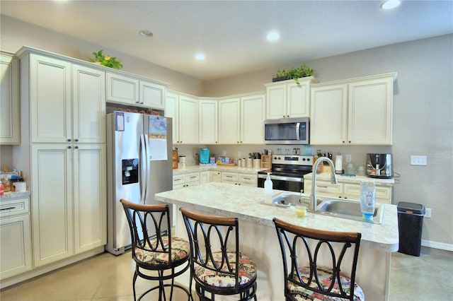 kitchen with a breakfast bar, sink, appliances with stainless steel finishes, a kitchen island with sink, and light tile patterned floors