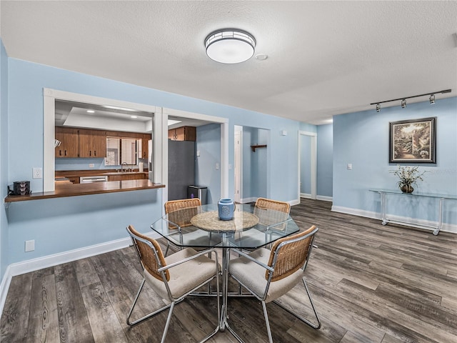 dining area with a textured ceiling, dark wood-type flooring, rail lighting, and sink