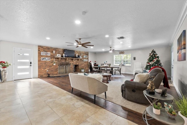 tiled living room with ceiling fan, a fireplace, a textured ceiling, and ornamental molding