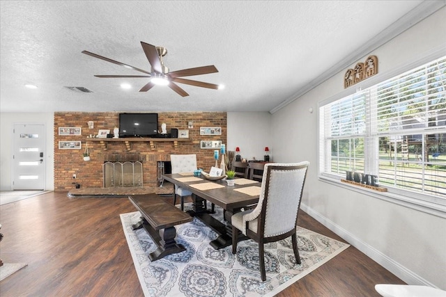 dining area featuring ceiling fan, a textured ceiling, hardwood / wood-style flooring, a fireplace, and ornamental molding