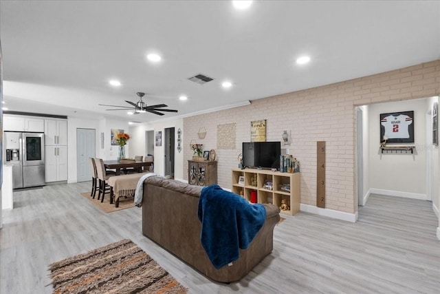 living room featuring light hardwood / wood-style flooring, ceiling fan, and brick wall