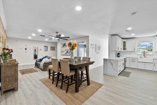 dining space featuring a textured ceiling, ceiling fan, sink, and light hardwood / wood-style flooring