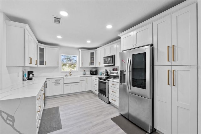 kitchen with light stone counters, stainless steel appliances, sink, white cabinets, and light hardwood / wood-style floors