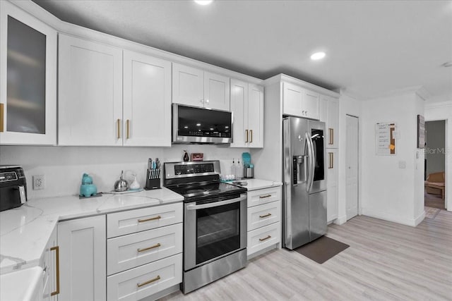 kitchen with light hardwood / wood-style flooring, light stone countertops, ornamental molding, appliances with stainless steel finishes, and white cabinetry