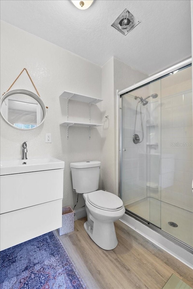 bathroom with a textured ceiling, hardwood / wood-style flooring, toilet, and a shower with shower door