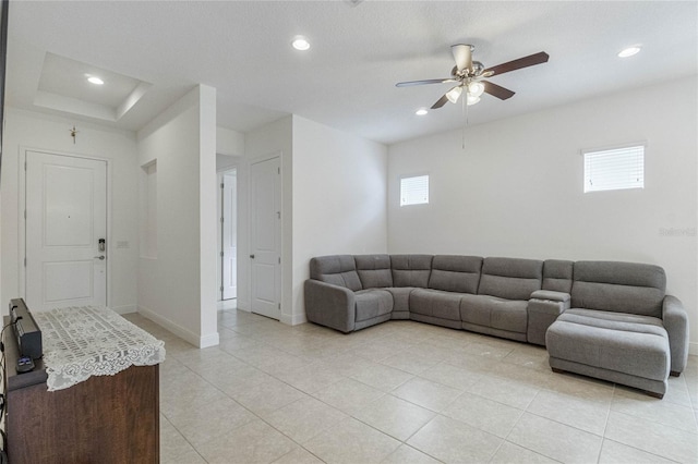 living room featuring a raised ceiling, light tile patterned flooring, ceiling fan, and a wealth of natural light