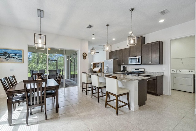 kitchen with stainless steel appliances, a kitchen breakfast bar, hanging light fixtures, and an island with sink