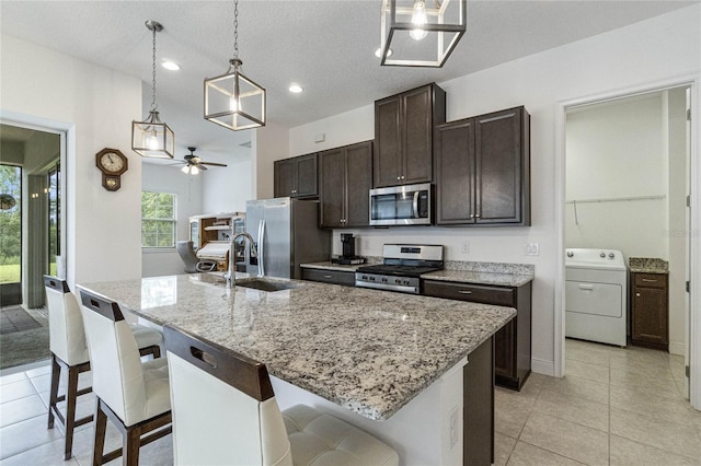 kitchen with washer / clothes dryer, a breakfast bar area, appliances with stainless steel finishes, hanging light fixtures, and an island with sink