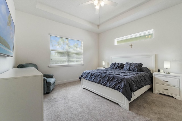 bedroom with ceiling fan, light carpet, and a tray ceiling