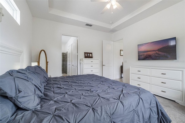 carpeted bedroom featuring ensuite bath, ceiling fan, and a tray ceiling