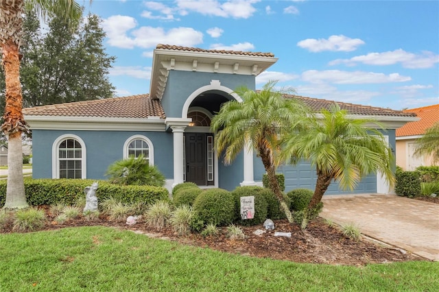 mediterranean / spanish home featuring driveway, an attached garage, a tiled roof, and stucco siding