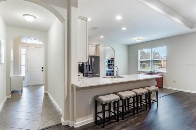 kitchen featuring stainless steel fridge, dark wood-type flooring, sink, white cabinetry, and a breakfast bar area