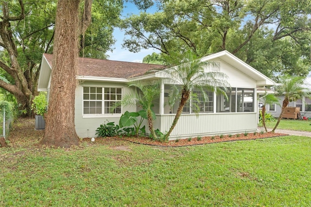 view of front of property with central air condition unit, a sunroom, a front lawn, and roof with shingles