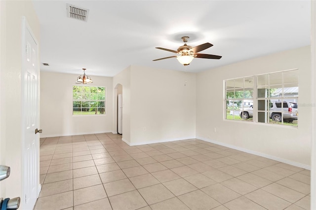 empty room with visible vents, arched walkways, baseboards, light tile patterned flooring, and ceiling fan with notable chandelier