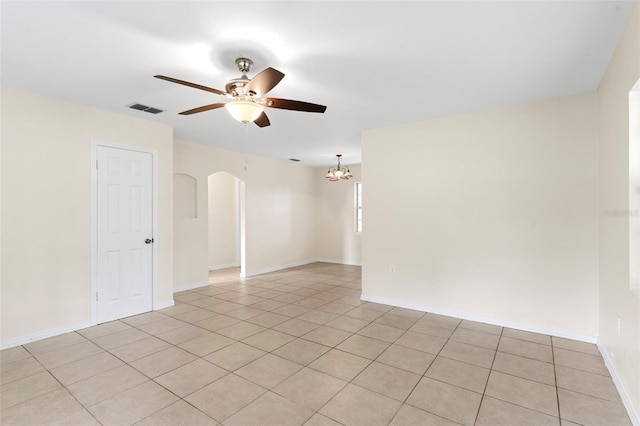 empty room featuring baseboards, visible vents, arched walkways, ceiling fan with notable chandelier, and light tile patterned flooring