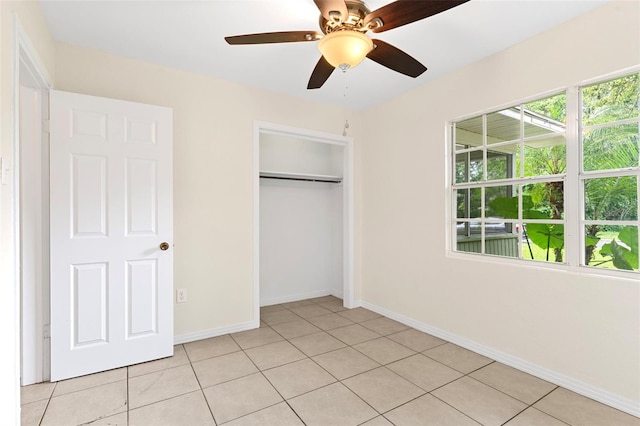 unfurnished bedroom with light tile patterned floors, ceiling fan, a closet, and baseboards