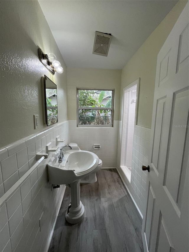 bathroom with visible vents, a wainscoted wall, wood finished floors, a shower stall, and tile walls