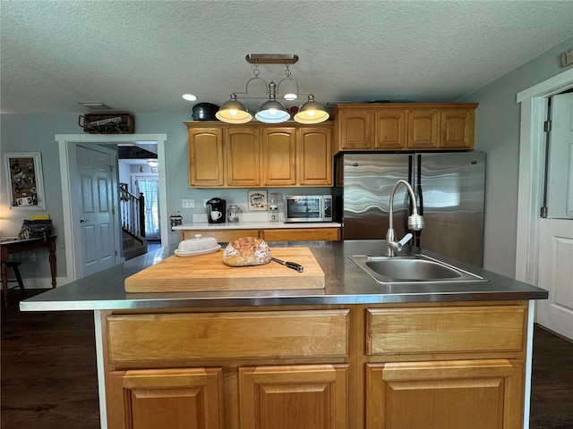 kitchen featuring appliances with stainless steel finishes, a textured ceiling, a center island with sink, and sink