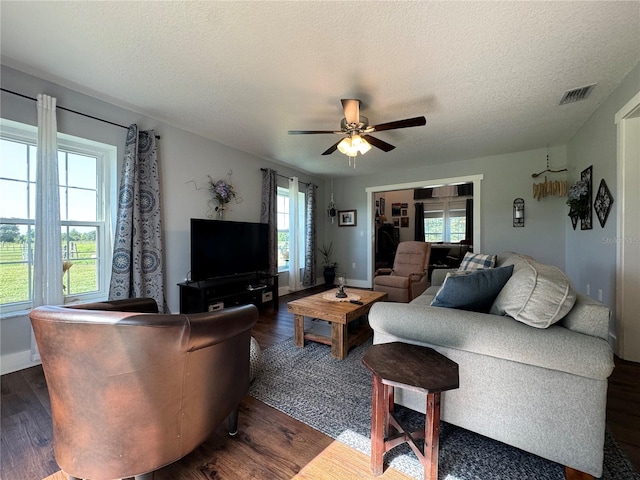 living room with ceiling fan, a textured ceiling, and dark wood-type flooring