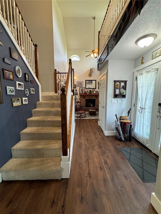 entrance foyer with ceiling fan, a towering ceiling, a textured ceiling, a fireplace, and dark hardwood / wood-style flooring