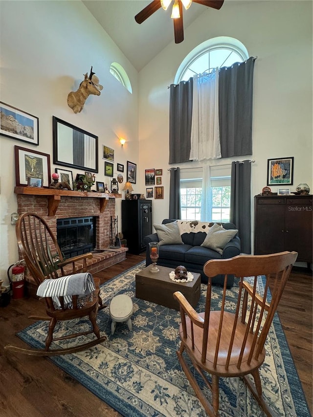 living room featuring ceiling fan, a fireplace, high vaulted ceiling, and dark wood-type flooring