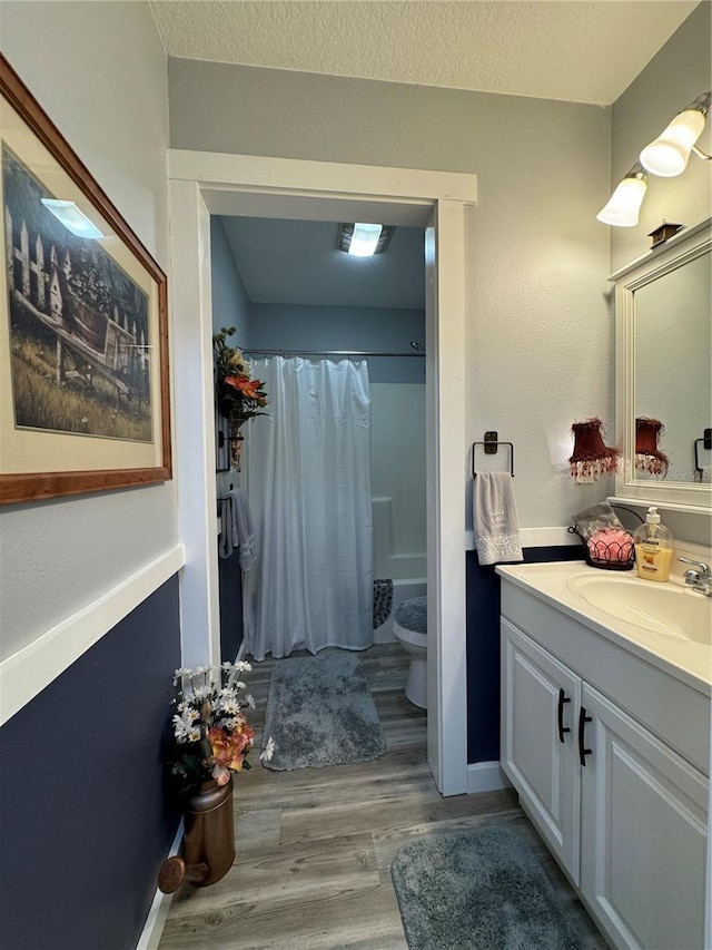 full bathroom featuring wood-type flooring, a textured ceiling, toilet, shower / bath combo with shower curtain, and vanity