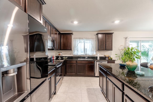 kitchen with sink, dark stone countertops, dark brown cabinets, light tile patterned floors, and appliances with stainless steel finishes