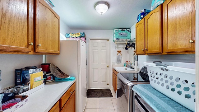 clothes washing area with sink, washing machine and dryer, cabinets, and light tile patterned floors