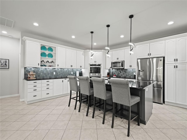 kitchen with appliances with stainless steel finishes, tasteful backsplash, a center island with sink, and light tile patterned flooring