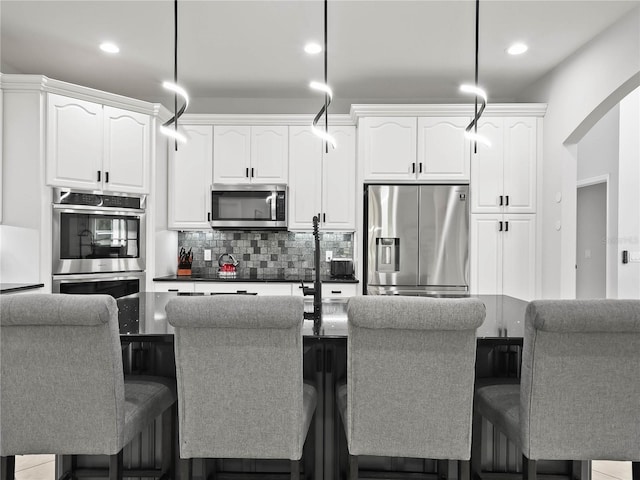 kitchen featuring pendant lighting, backsplash, a breakfast bar, stainless steel appliances, and white cabinets