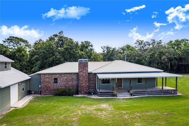 rear view of house featuring covered porch, metal roof, a lawn, and a chimney