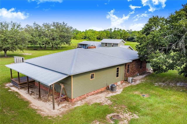 back of property with driveway, central AC unit, metal roof, and a yard