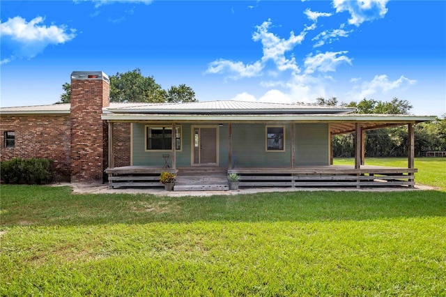 rear view of house with brick siding, a chimney, covered porch, a lawn, and metal roof