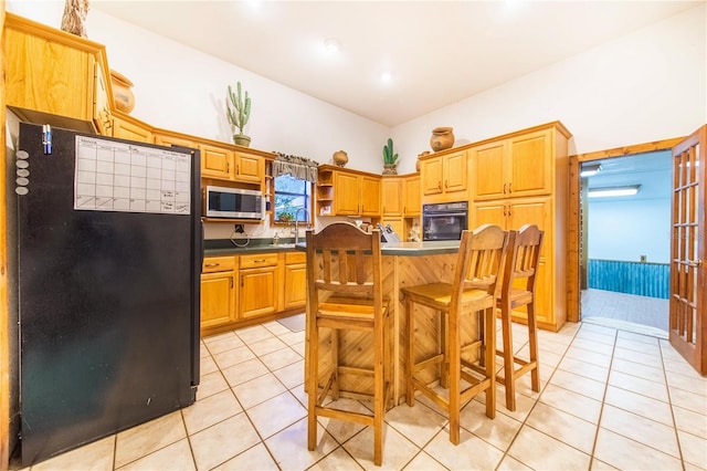 kitchen with sink, black appliances, a kitchen bar, and light tile patterned floors