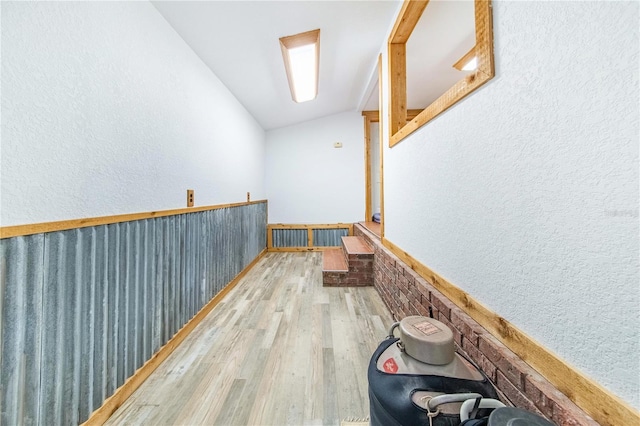 interior space featuring a textured wall, wainscoting, vaulted ceiling, and light wood-style flooring