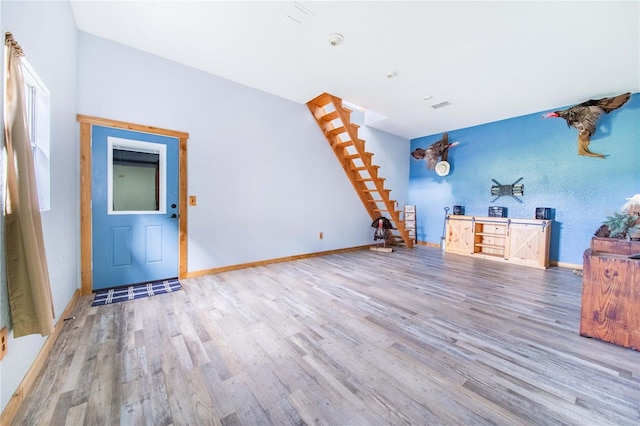 unfurnished living room with visible vents, stairway, baseboards, and wood finished floors