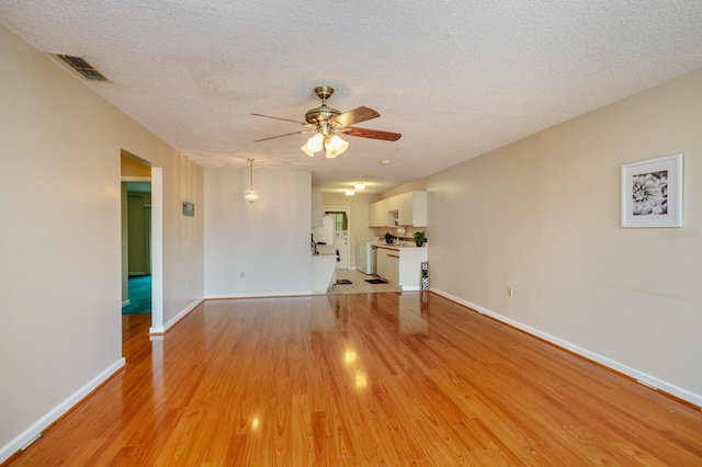 unfurnished living room with a textured ceiling, light hardwood / wood-style flooring, and ceiling fan