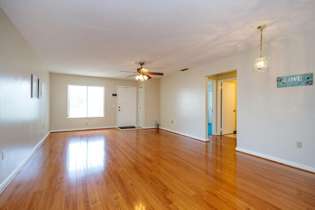 empty room featuring ceiling fan with notable chandelier, a textured ceiling, and light hardwood / wood-style flooring