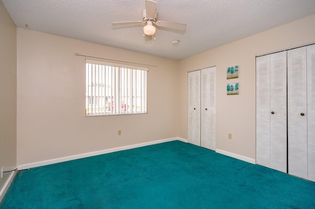 unfurnished bedroom with ceiling fan, carpet, a textured ceiling, and multiple closets