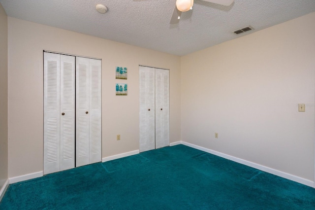 unfurnished bedroom with a textured ceiling, carpet flooring, ceiling fan, and multiple closets