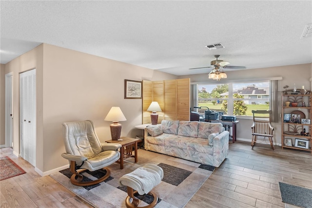 living room with a textured ceiling, light hardwood / wood-style flooring, and ceiling fan