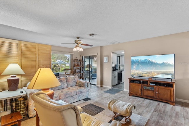 living room with a textured ceiling, ceiling fan, and light hardwood / wood-style floors