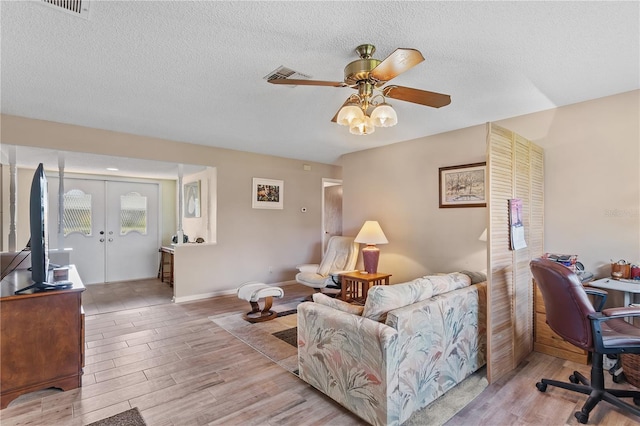 living room featuring light wood-type flooring, ceiling fan, a textured ceiling, and french doors