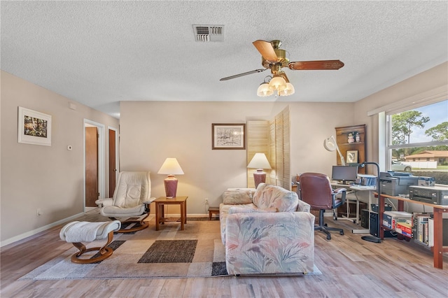 living room featuring ceiling fan, light hardwood / wood-style floors, and a textured ceiling