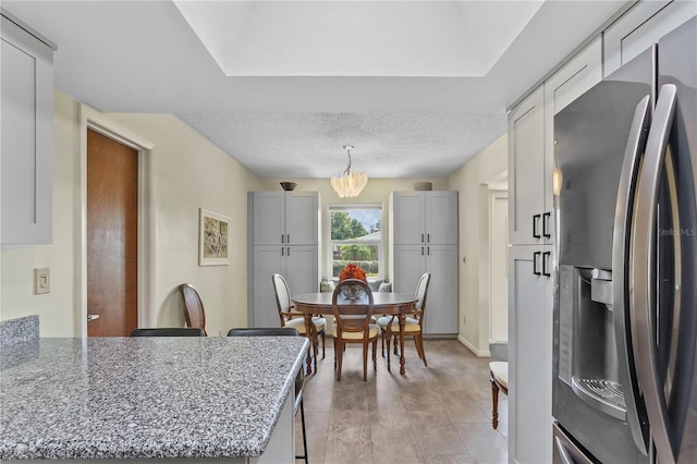 kitchen featuring stainless steel refrigerator with ice dispenser, stone countertops, a textured ceiling, and a chandelier