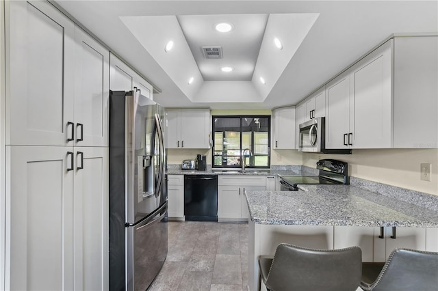 kitchen with a tray ceiling, black appliances, and white cabinetry